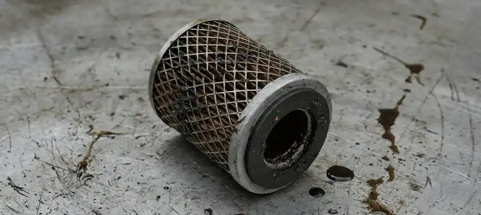Clogged diesel fuel filter cartridge covered in debris and sludge on a workbench.